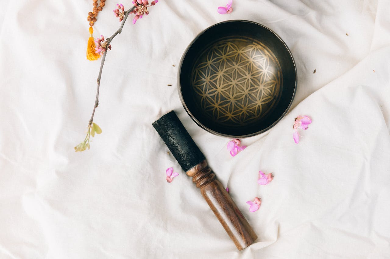 A Tibetan singing bowl on a white fabric surrounded by pink petals and branch, creating a serene atmosphere.
